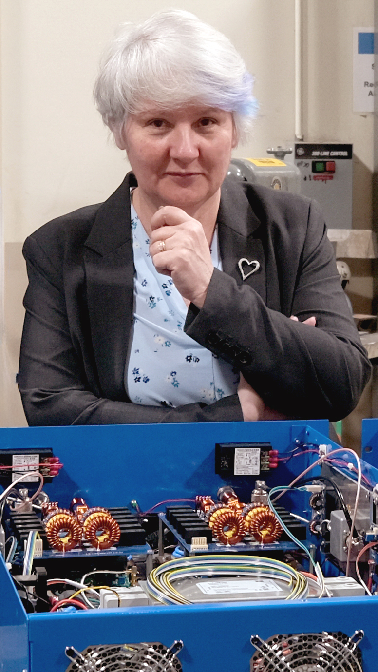 A woman looking into the camera, with a box of electronics on the table in front of her